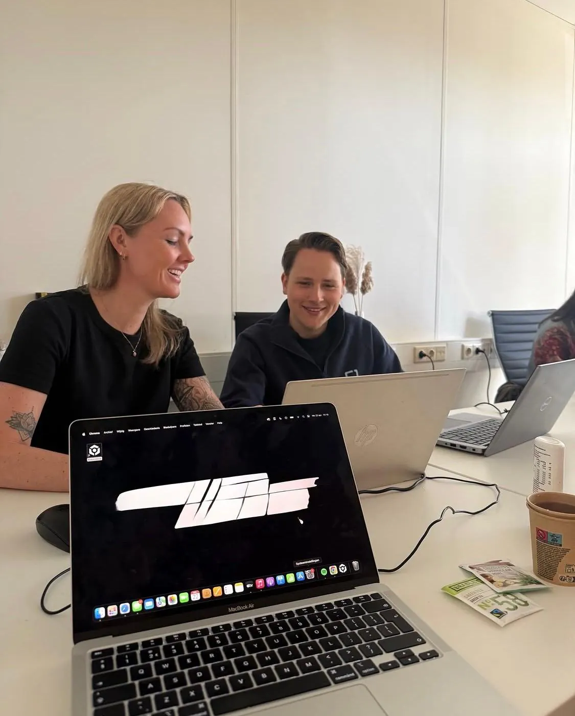 Twee collega's lachen achter hun laptop op kantoor