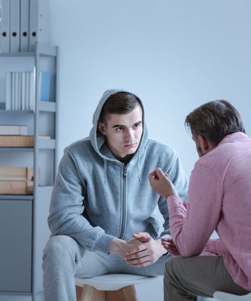 A psychology specialist explaining an action plan for recovery to a troubled teenage boy during an individual therapy session.